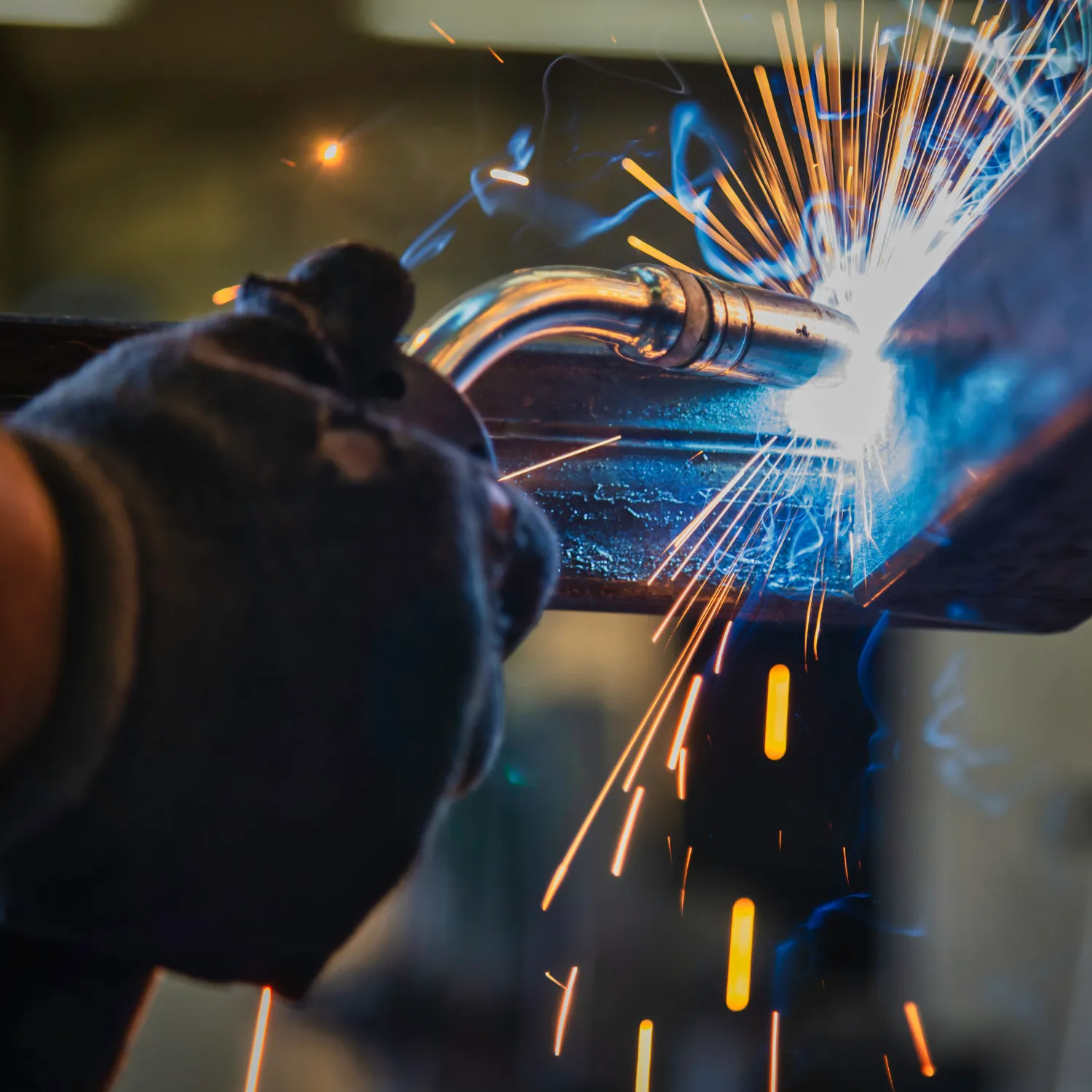 Close-up of a person welding metal with sparks flying and blue smoke visible.