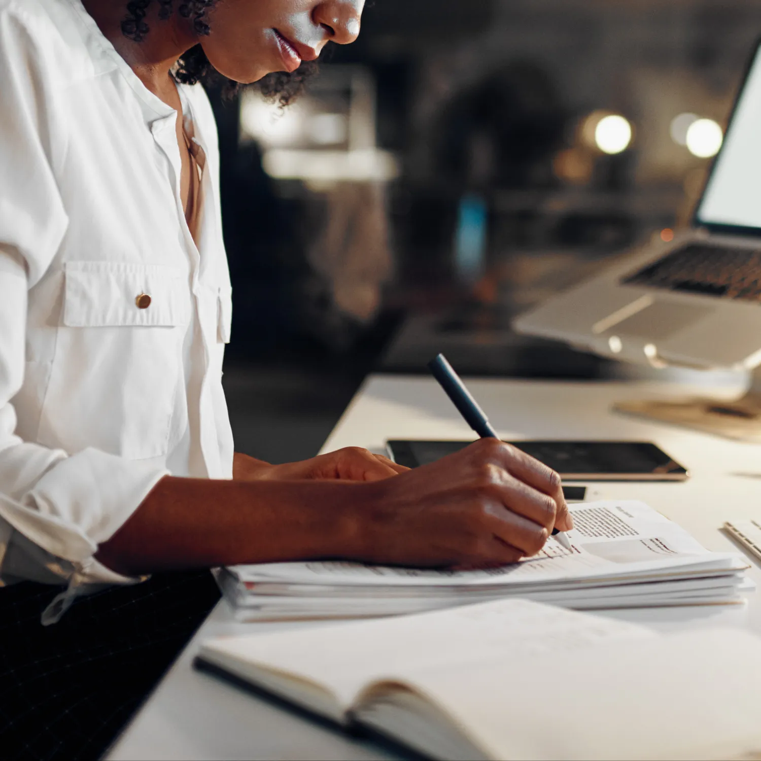 Person writing notes on papers at a desk with a laptop and tablet nearby.