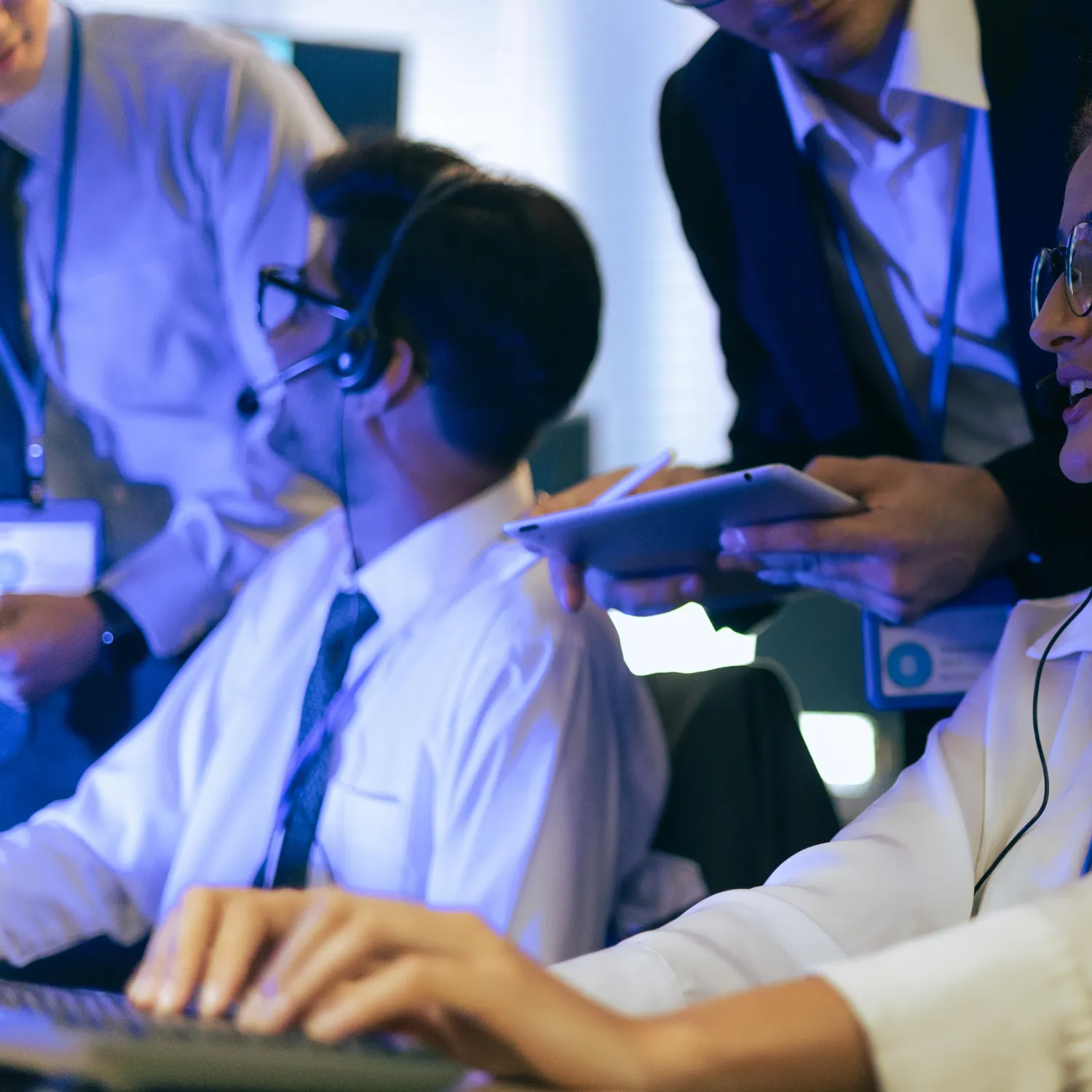 Customer service team members wearing headsets working together with one person holding a tablet.