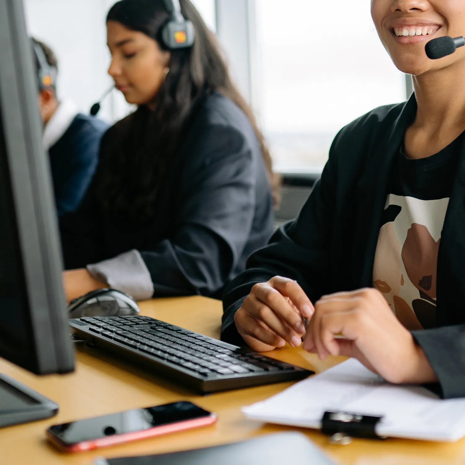 Smiling customer service representatives wearing headsets working at computers in an office.