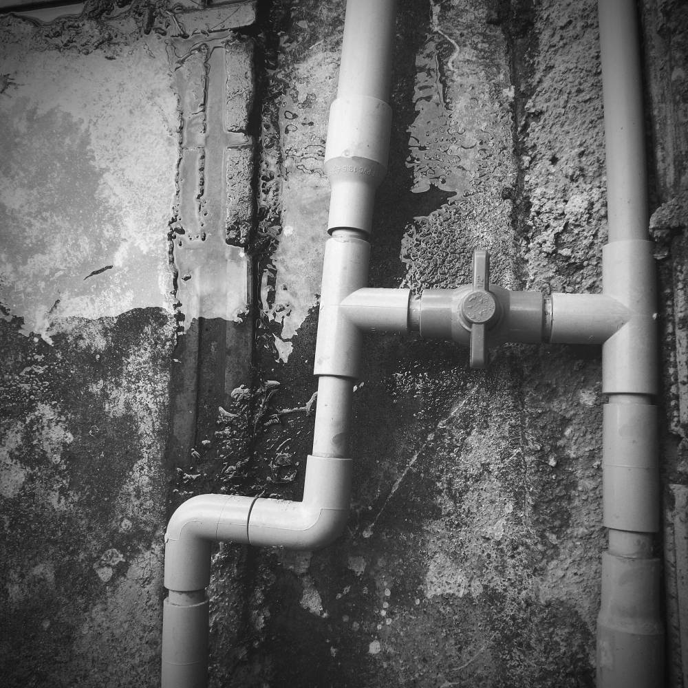 Kunststof waterleidingen met een kraan gemonteerd op een ruwe muur met waterresten.