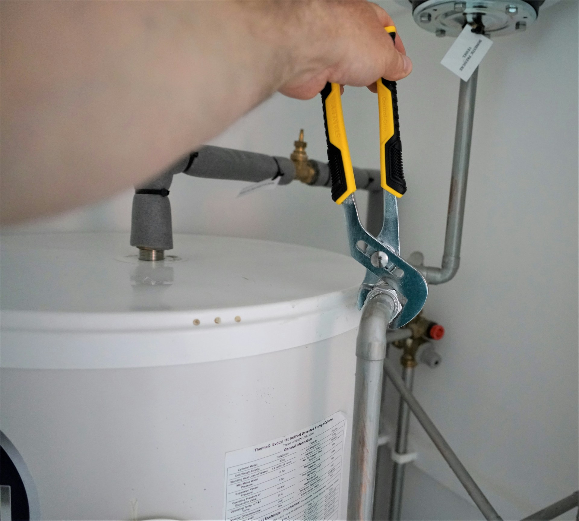 Hand met een waterpomptang die een pijp aan een witte boiler vastdraait.