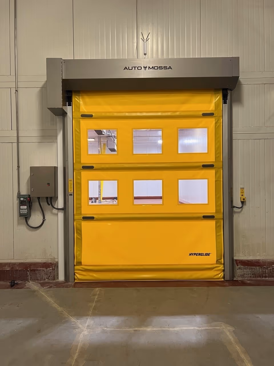 Industrial yellow Auto Mossa Hyperglide roller door with six small rectangular windows in a warehouse.