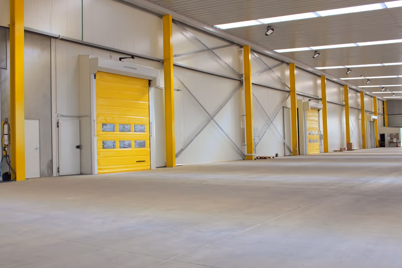 Spacious, empty industrial warehouse interior with yellow roller doors and concrete floor.
