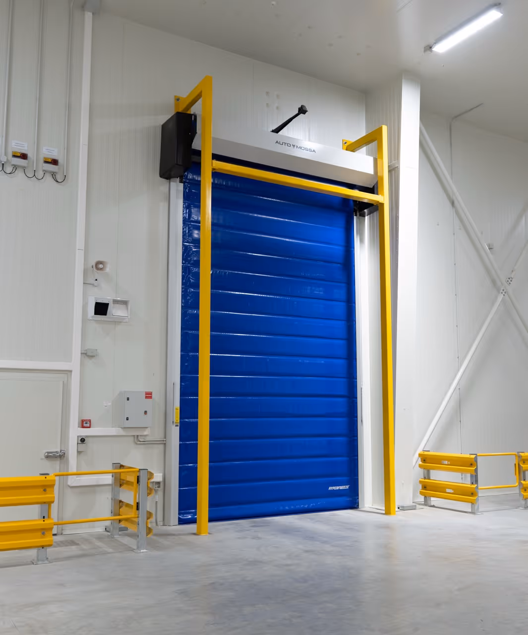 Large blue industrial roller door with yellow safety frame inside a clean warehouse.