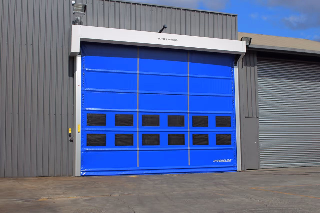 Blue industrial roller door with rectangular black windows, mounted on grey corrugated metal building.