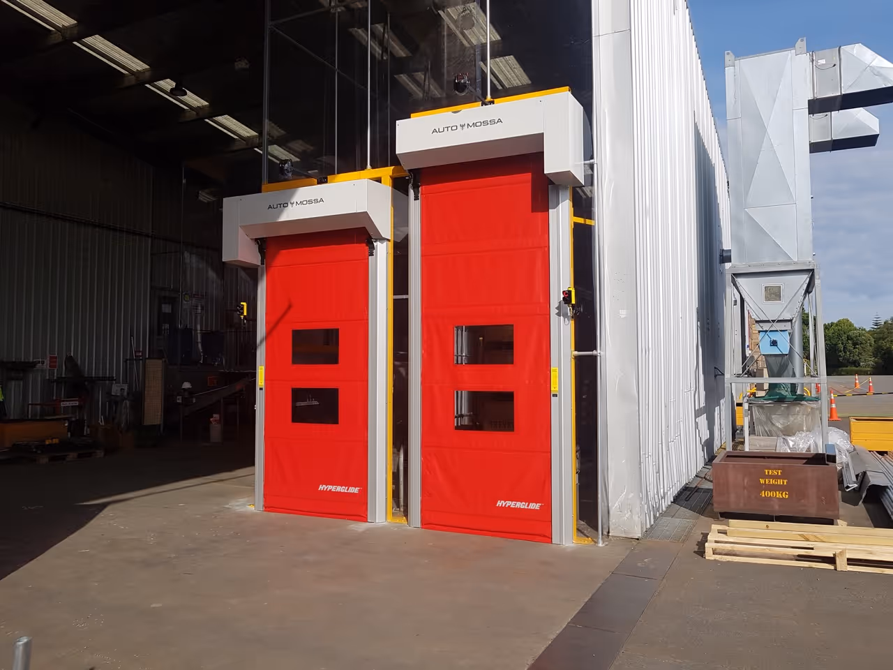 Two red industrial fabric doors with windows installed side by side on a warehouse building.