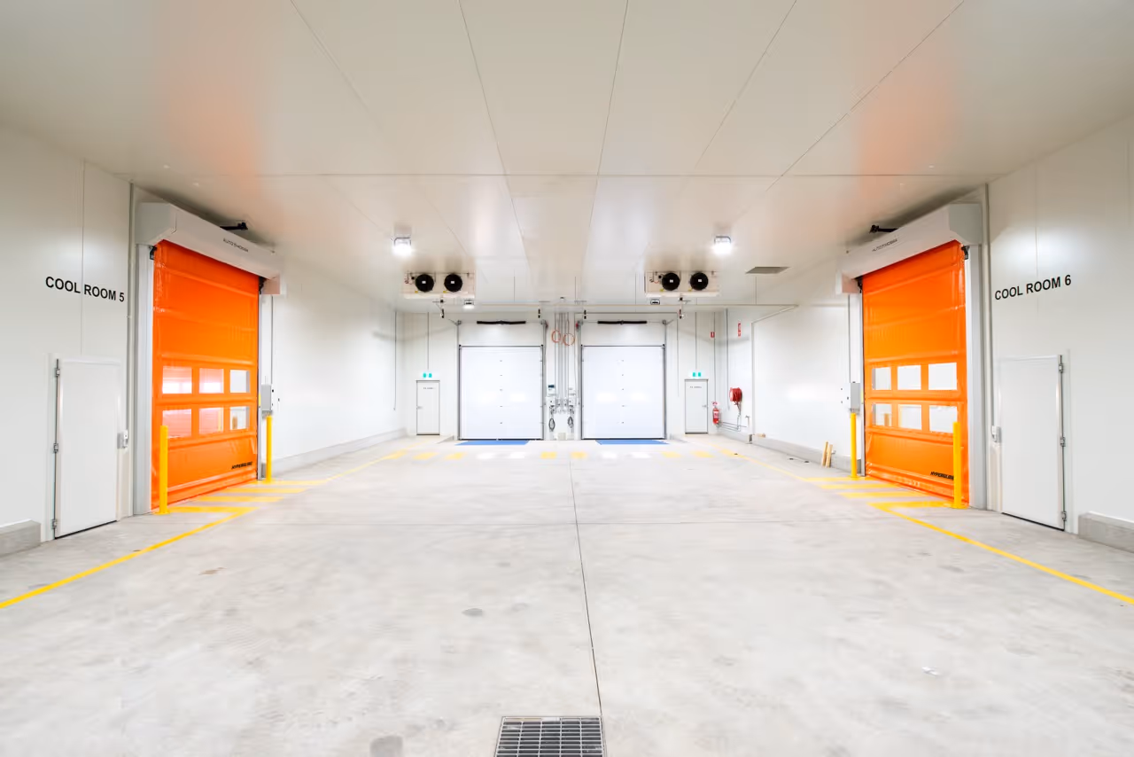 Interior of a clean industrial cold storage facility with two large orange roller doors labelled Cool Room 5 and Cool Room 6.