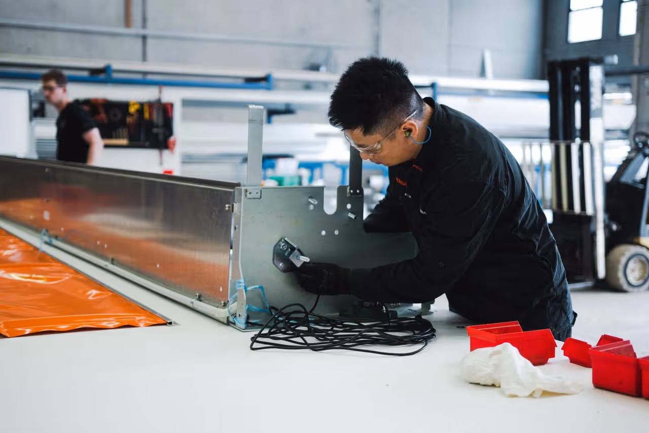 Worker wearing safety glasses and earplugs assembling metal equipment in a workshop.