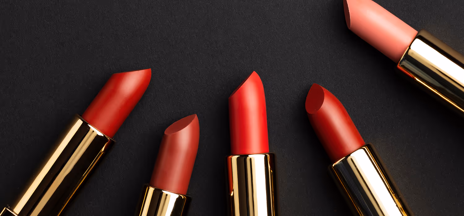 Fünf Lippenstifte in verschiedenen Rottönen und einem pinken Ton auf schwarzem Hintergrund.