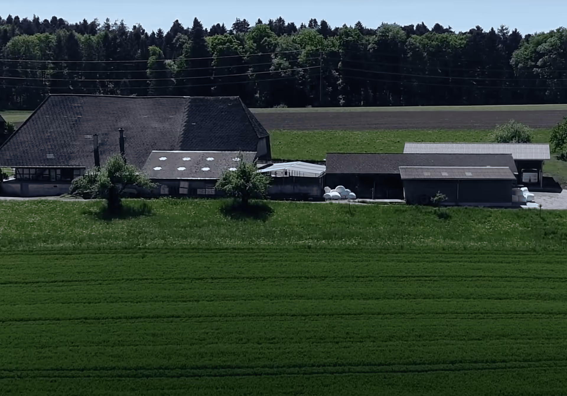 Landwirtschaftlicher Hof mit mehreren Gebäuden, umgeben von grünen Feldern und Bäumen.