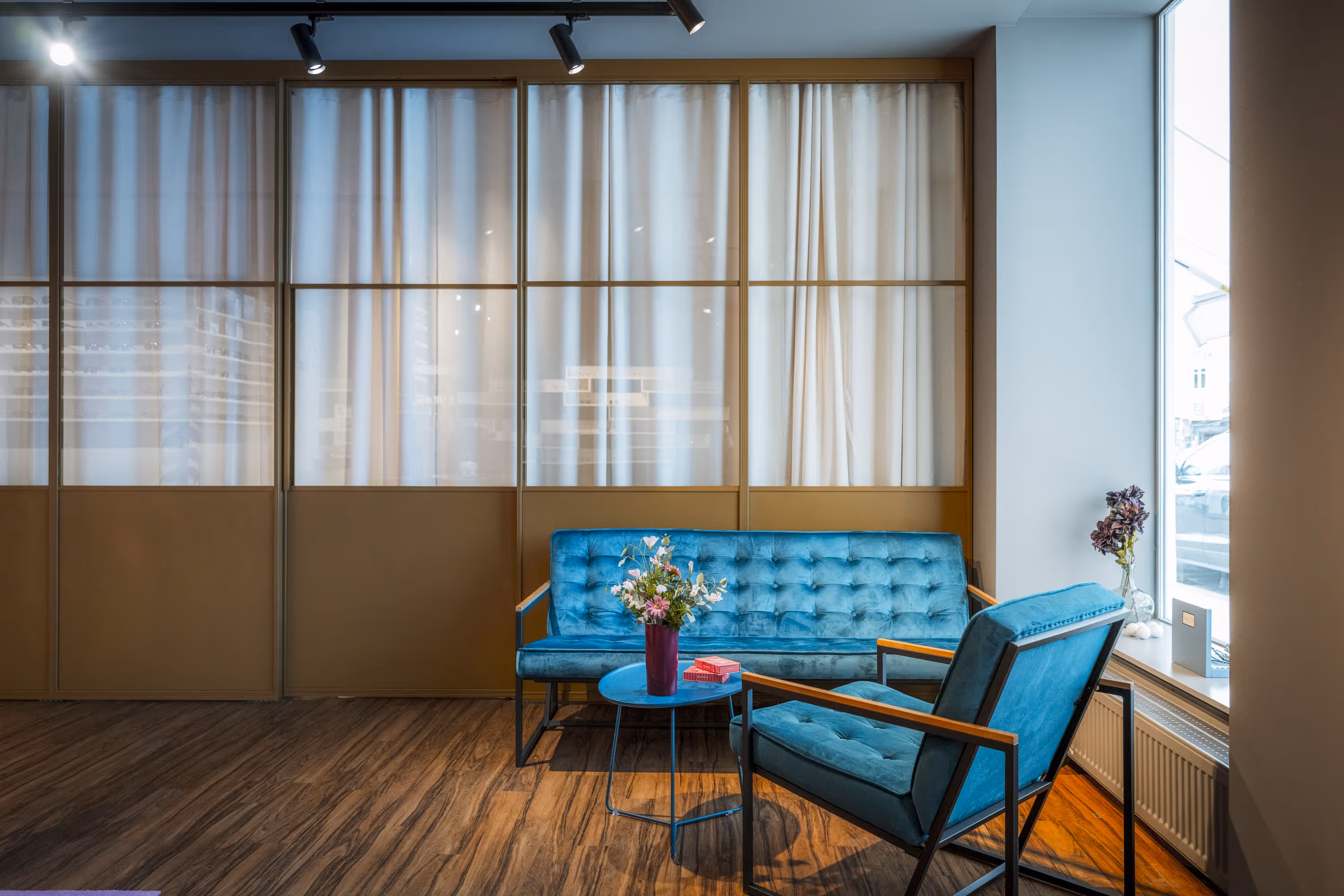 Moderner Warteraum mit blauem Sofa und Sessel, kleinem runden Tisch mit Blumenstrauß und Holzfußboden.