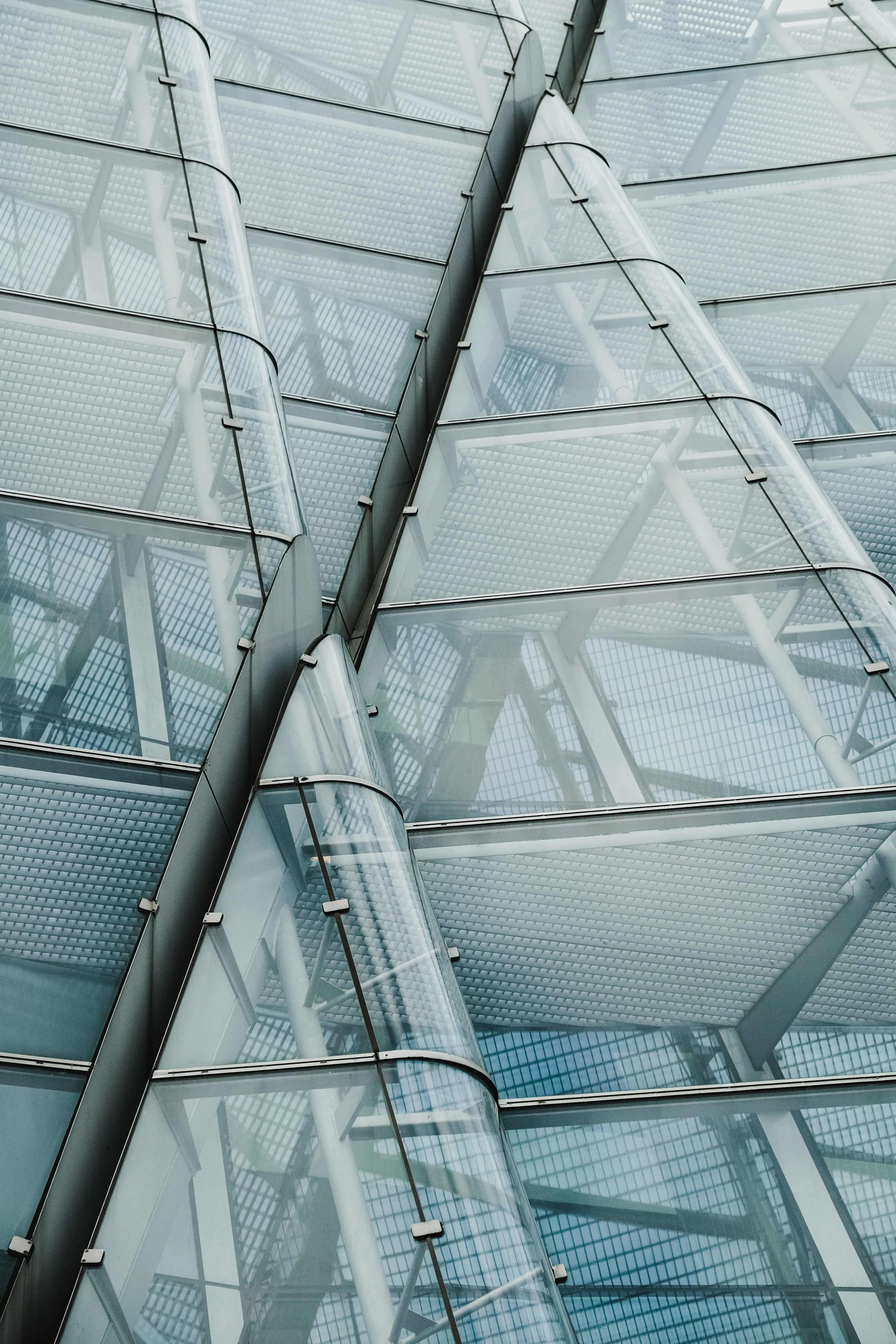 Close-up of a modern glass building facade with angled reflective panels and visible structural supports.