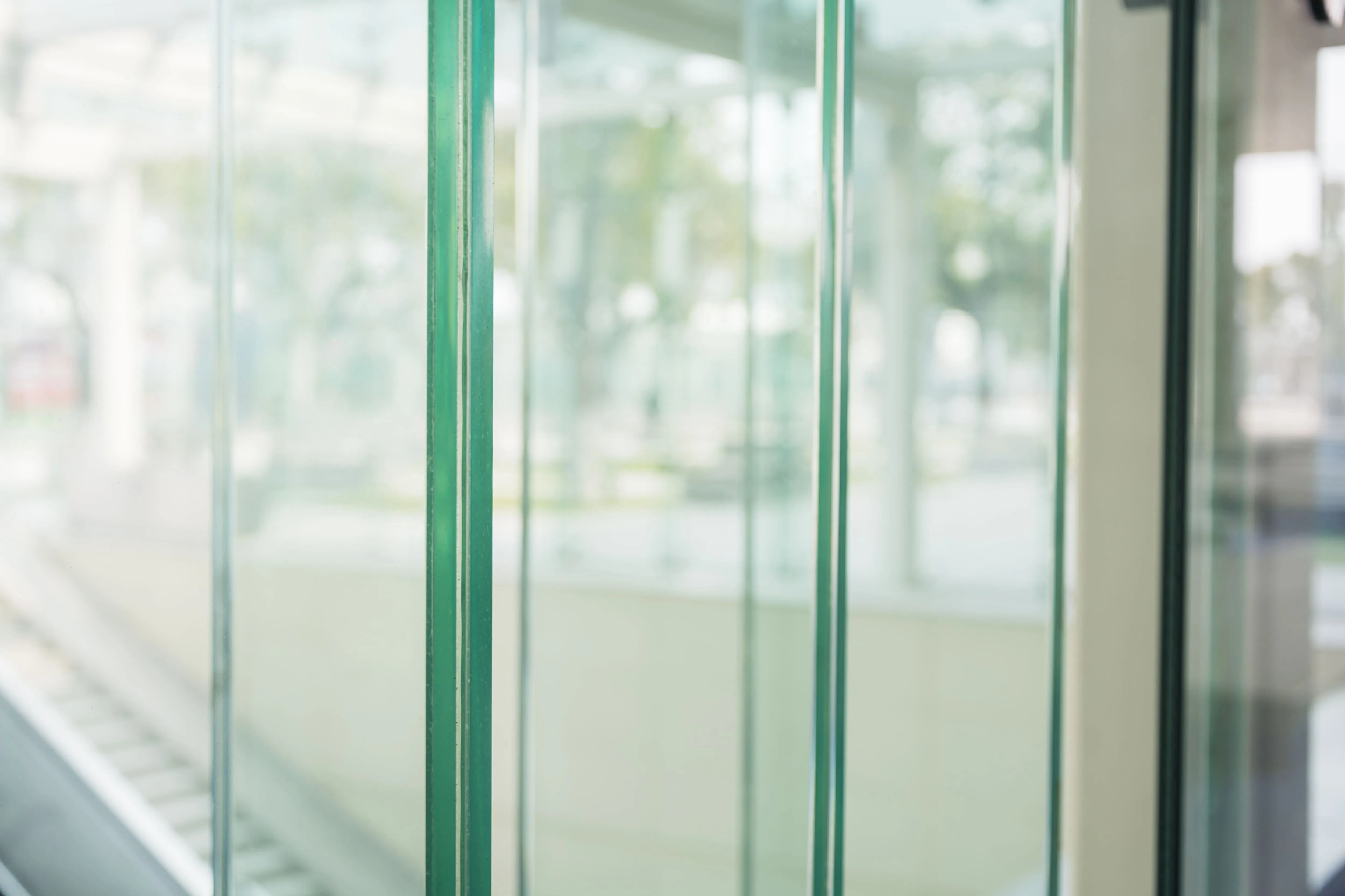 Close-up of multiple clear laminated glass panels with green edges in an indoor setting.