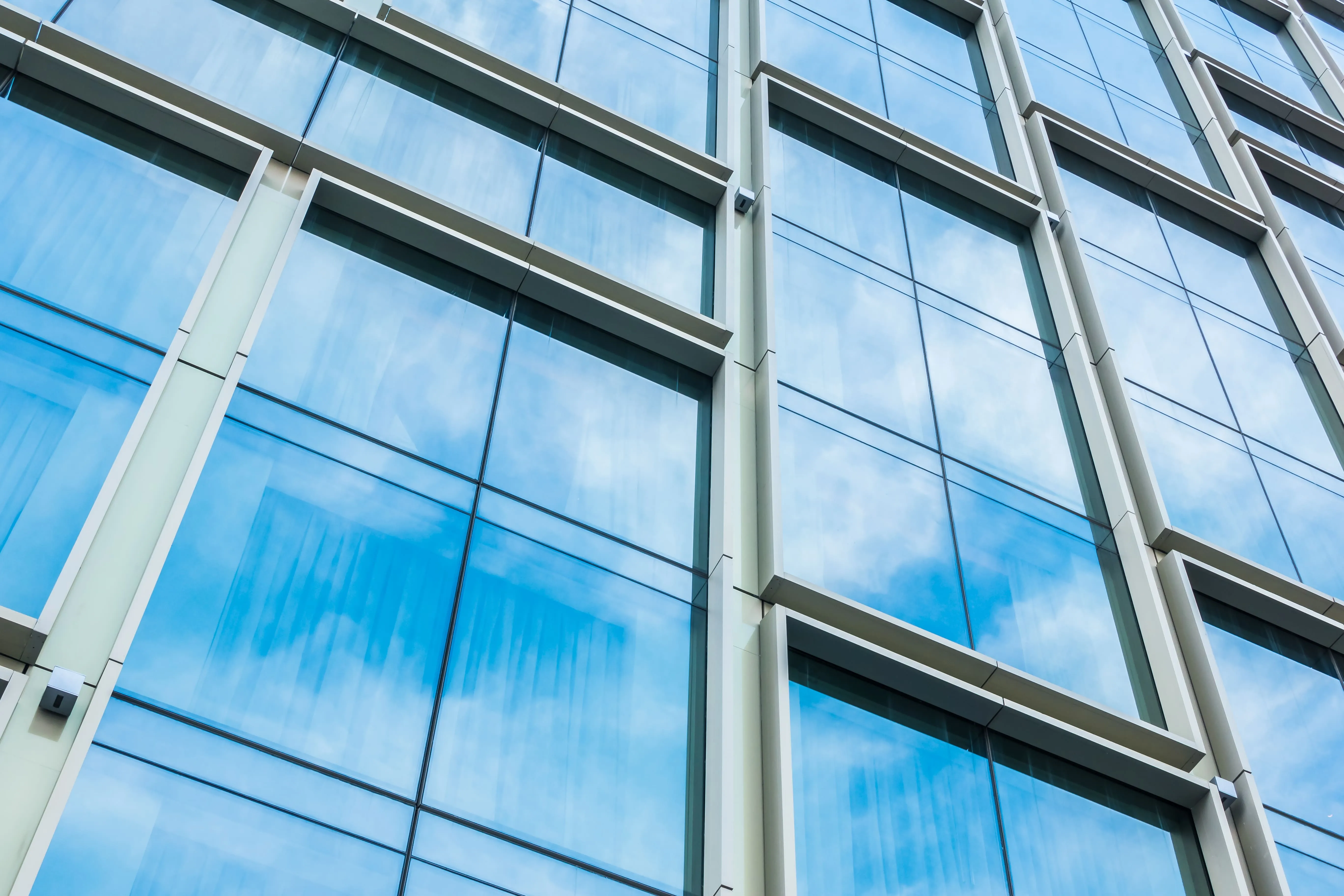 Glass exterior facade of a modern building reflecting the blue sky and clouds.