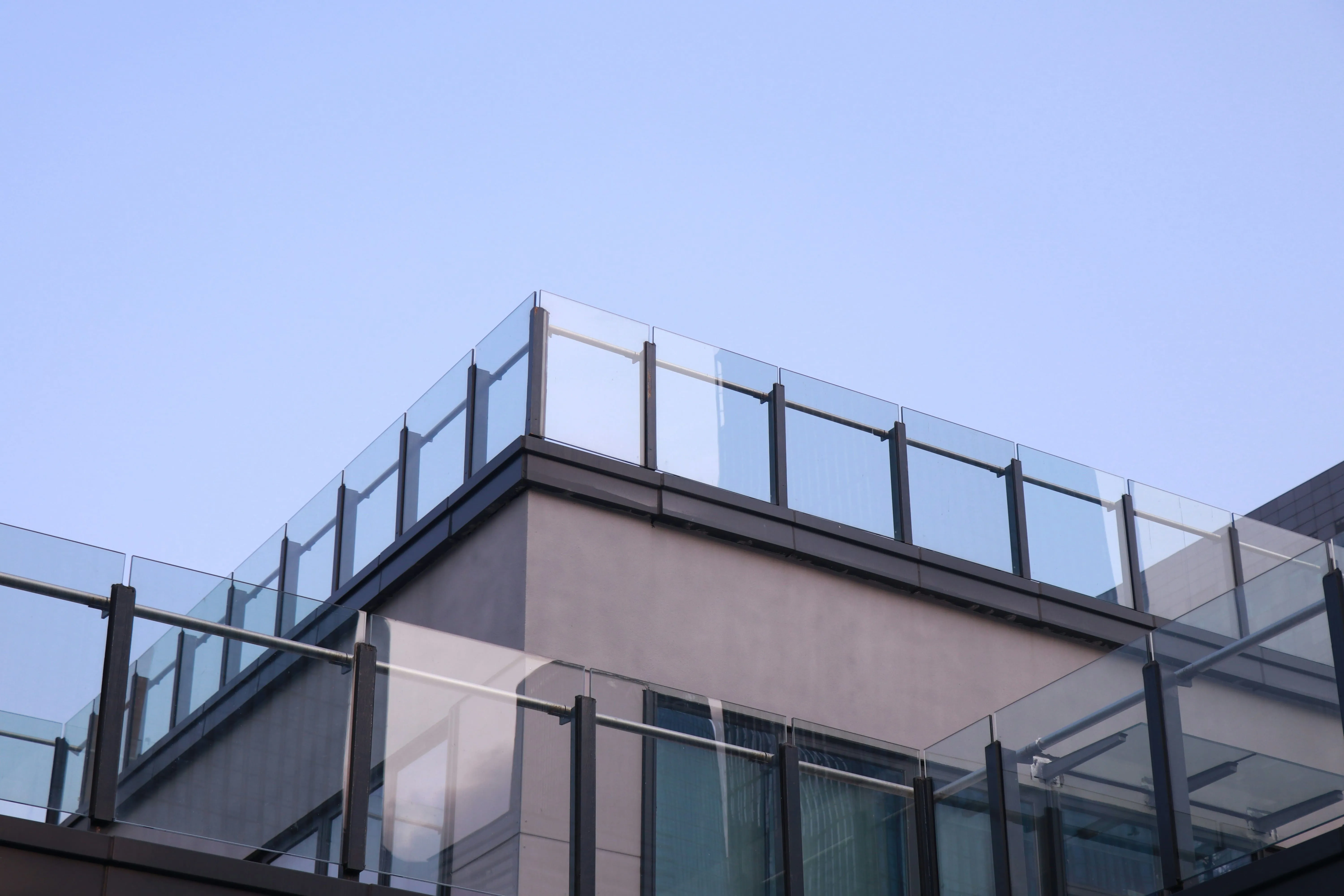 Modern building corner with glass balcony railings under clear blue sky.