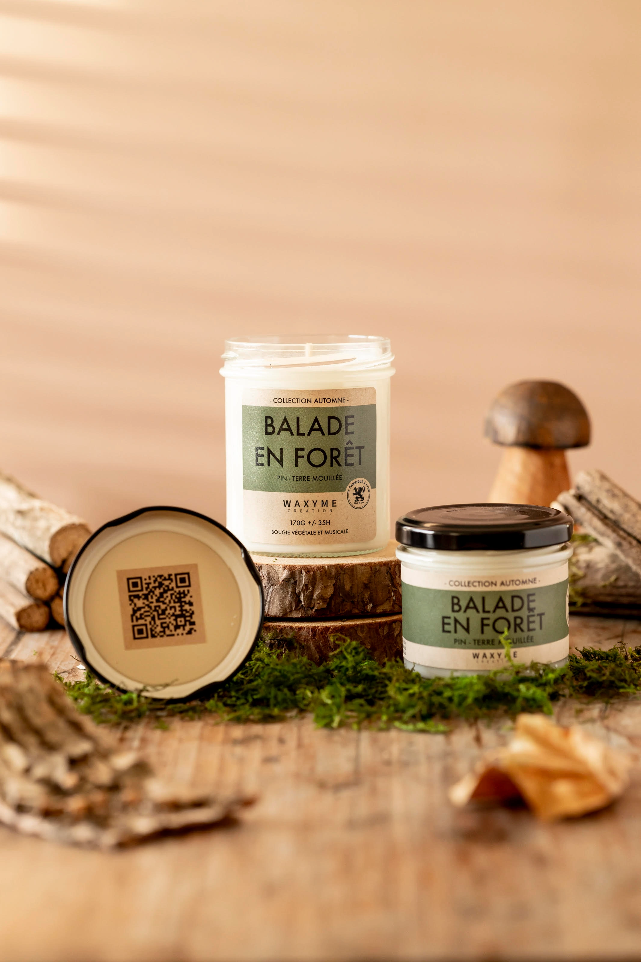 Shooting d'une bougie naturelle et musicale de la marque Waxyme dans le thème de l'automne, de la nature. Elle est posée sur des rodins de bois et entourée d'herbes, de bâtons, de feuilles, de champignons.