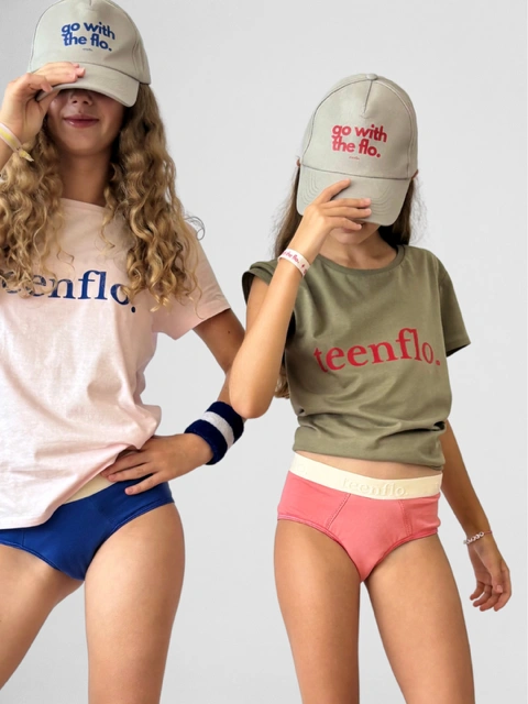 Deux adolescentes posant pour Teenflo, une marque de sous-vêtements menstruels pour ados. Elles portent un t-shirt et une casquette de la même marque.