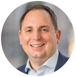 Porträt eines lächelnden Mannes mit kurzem braunem Haar in weißem Hemd und dunklem Sakko.