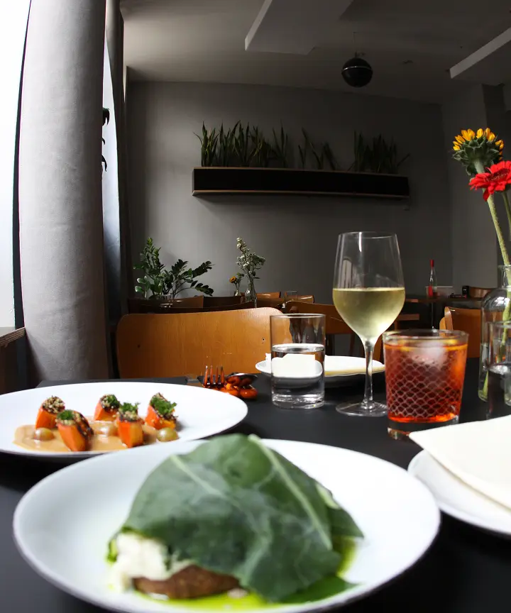 Tisch mit zwei Tellern mit Gourmetgerichten, einem Glas Weißwein und einem Cocktail in einem Restaurant.