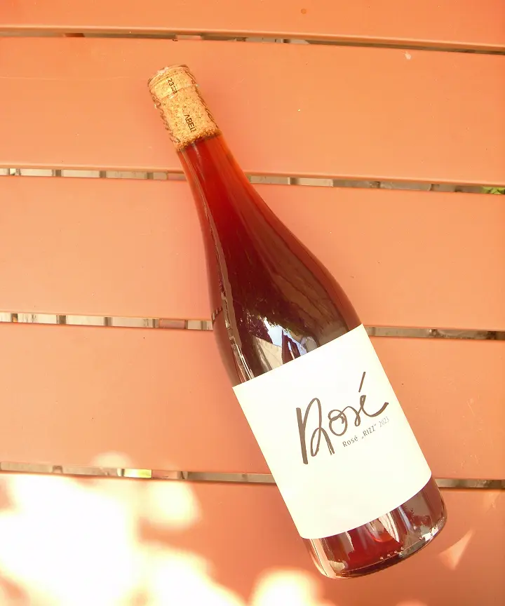 Flasche Roséwein mit weißem Etikett liegt auf braunem Lattenrost im Freien.