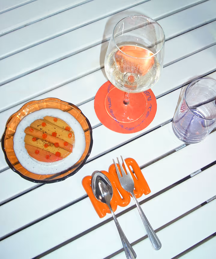 Teller mit Dessert, Weinglas auf rotem Untersetzer, Wasserglas und Besteck auf weißem Tisch.