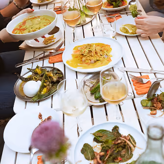 Menschen, die im Freien essen und sich an einem weiß gedeckten Tisch gemeinsam Gerichte und Gläser Weißwein teilen.