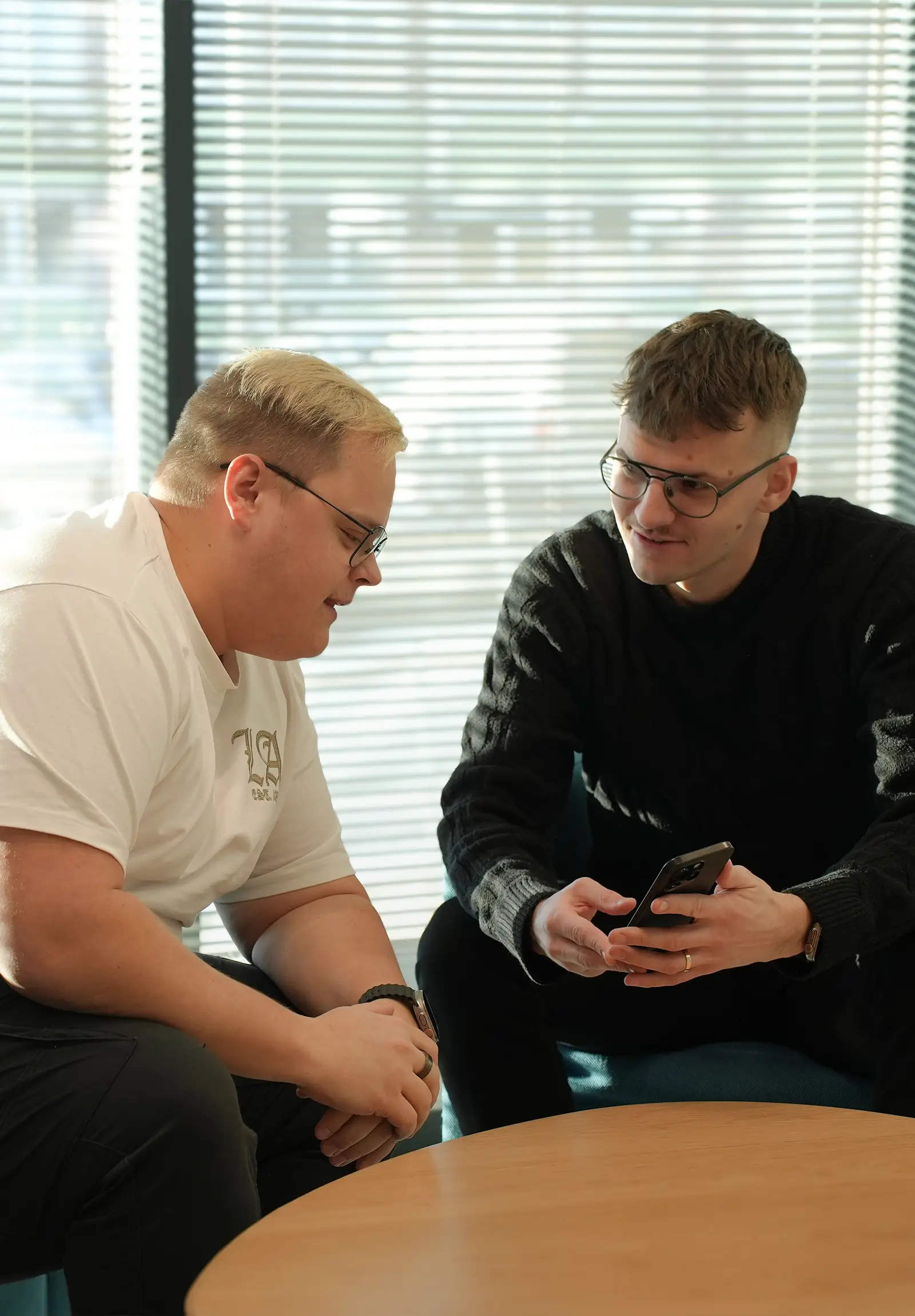 Kaks meest istuvad laudade taga ja vaatavad nutitelefoni ning vestlevad.