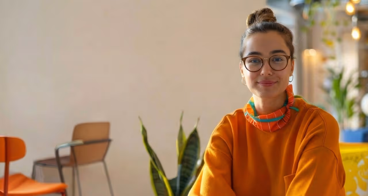Woman in an orange jumper sitting on a yellow lounge in a modern office.