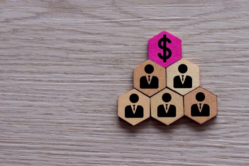 Hexagon wooden shapes on a table with a person icon on 5 of them and a dollar sign on one.