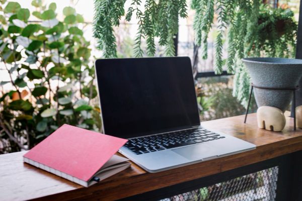 A professional setting showing a laptop and a handwritten journal on a wooden desk, symbolizing the blend of digital and traditional learning tools in a natural, bright environment.