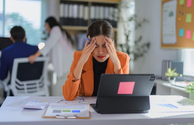 Stressed Asian businesswoman having headache while working with laptop in office