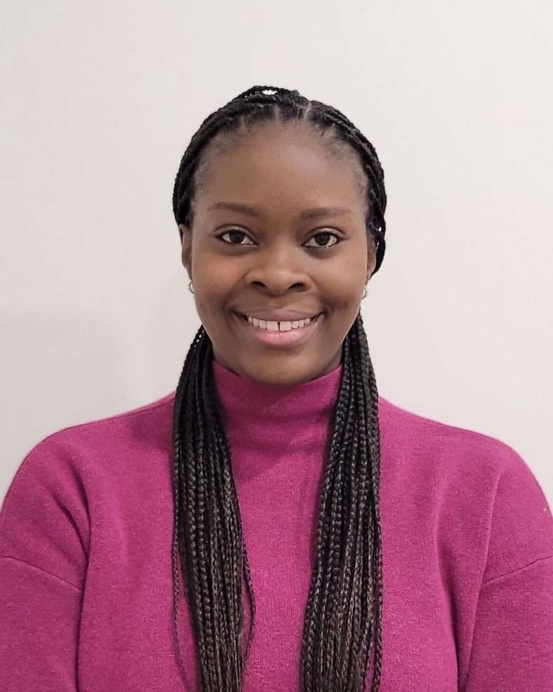 Woman with braided hair wearing a mustard turtleneck sweater sitting on a black chair in a modern indoor setting.