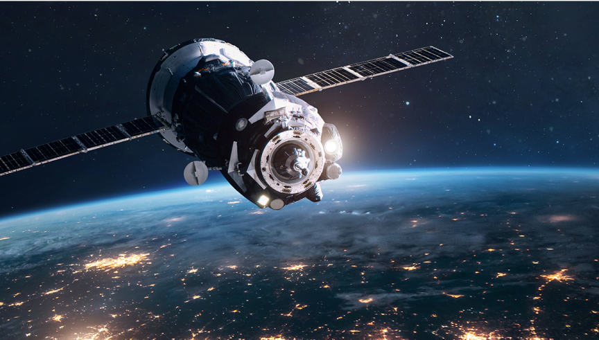 Satellite with extended solar panels orbits above Earth at night, with city lights glowing along the planet’s curved horizon.