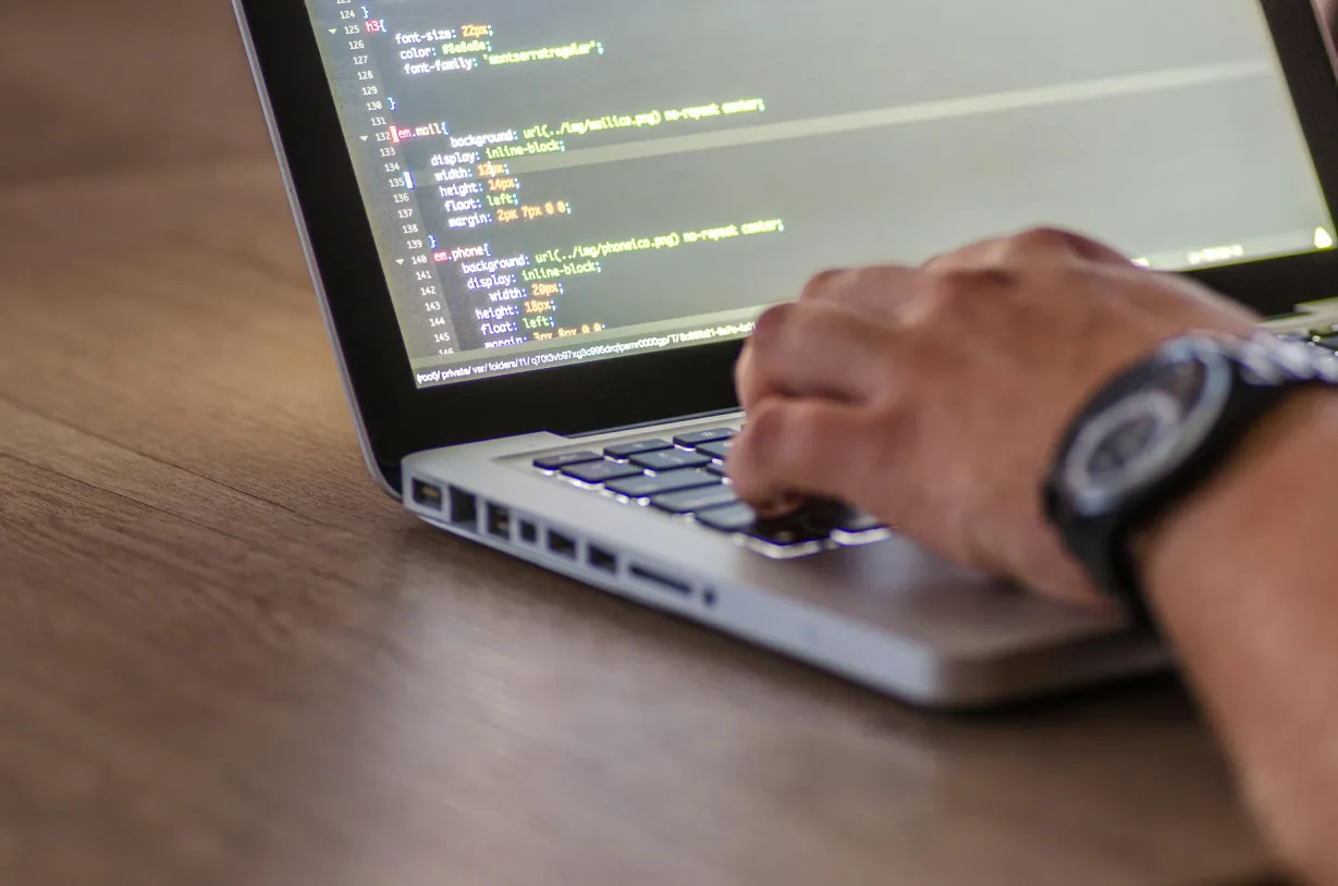 Close-up of hands typing on a laptop keyboard, with lines of code visible on the screen.