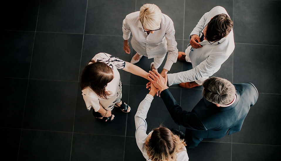 Overhead view of five business colleagues standing in a circle and stacking their hands together in a team huddle.
