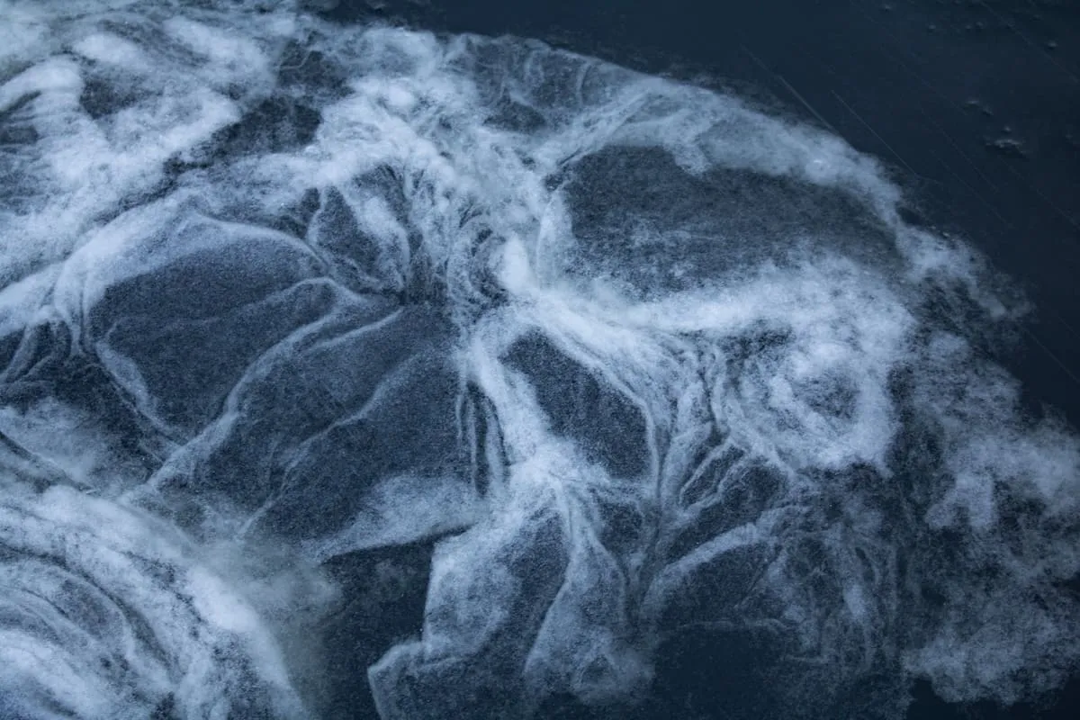 Close-up of delicate ice patterns and frost formations on a dark icy surface.