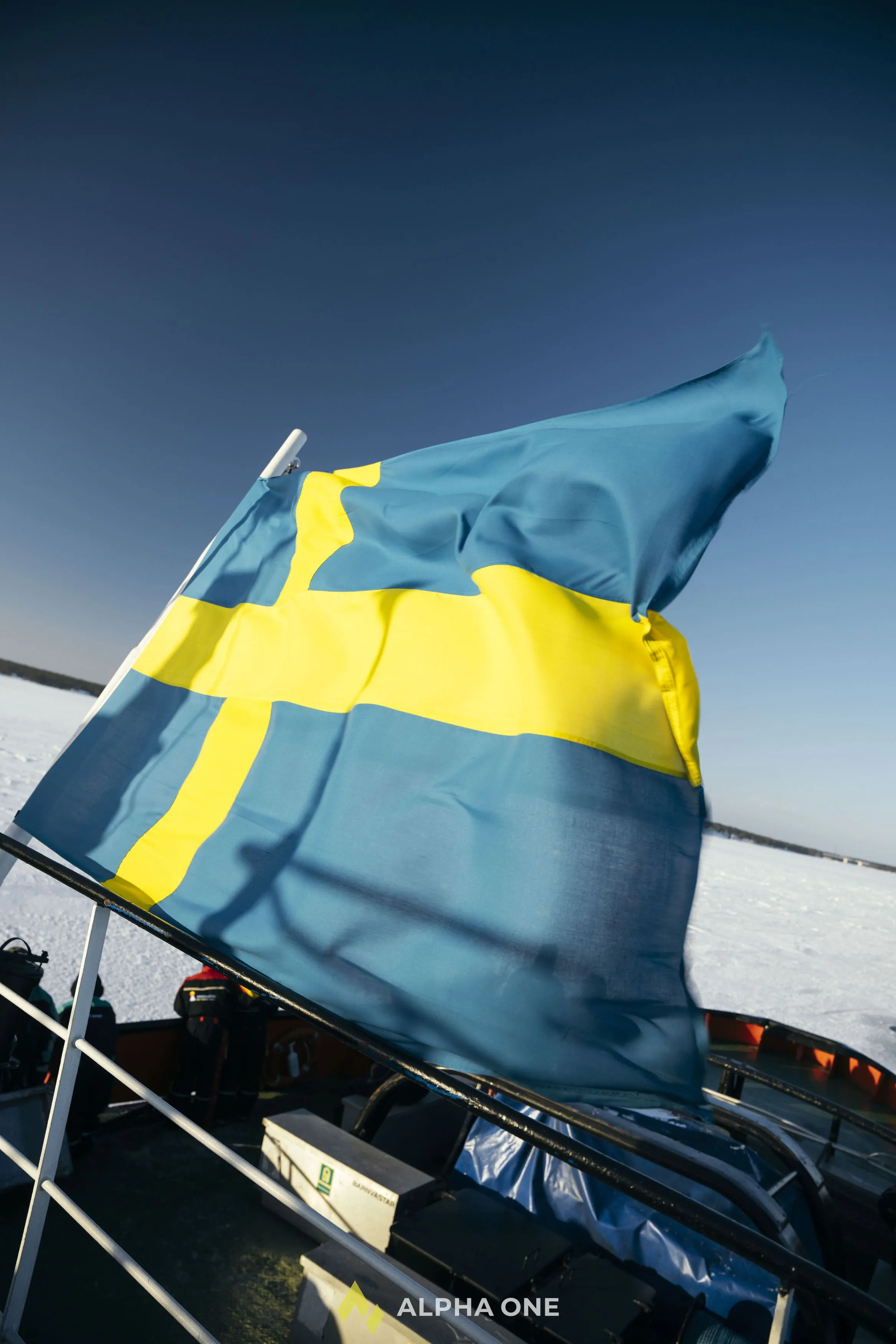 Swedish flag waving on a boat in a snowy, frozen landscape under a clear blue sky.