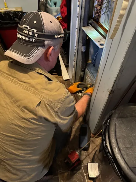 Man wearing a Chevrolet cap and gloves working on electrical wiring inside a panel.