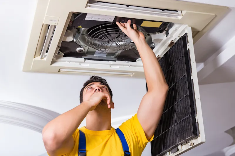 Technician inspecting and repairing a ceiling-mounted air conditioning unit.