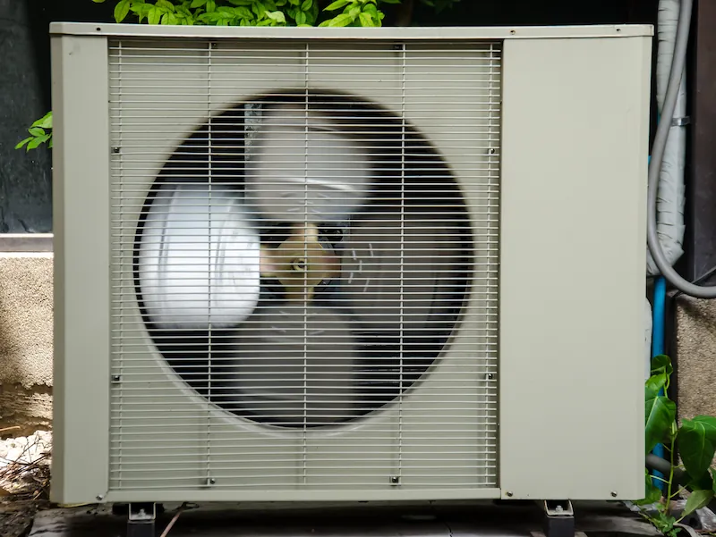 Outdoor air conditioning unit with a large fan behind a metal grille.