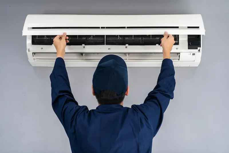 Technician in navy uniform servicing a wall-mounted air conditioner.