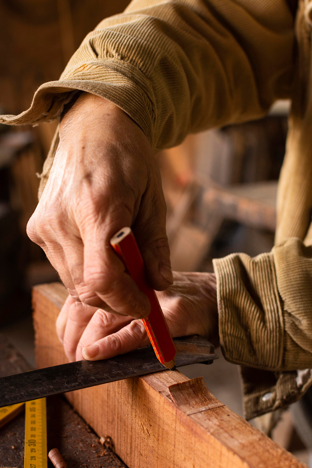 Close-up of a person's hands marking a wooden plank with a red pencil using a metal ruler in a woodworking setting. Source: Freepik