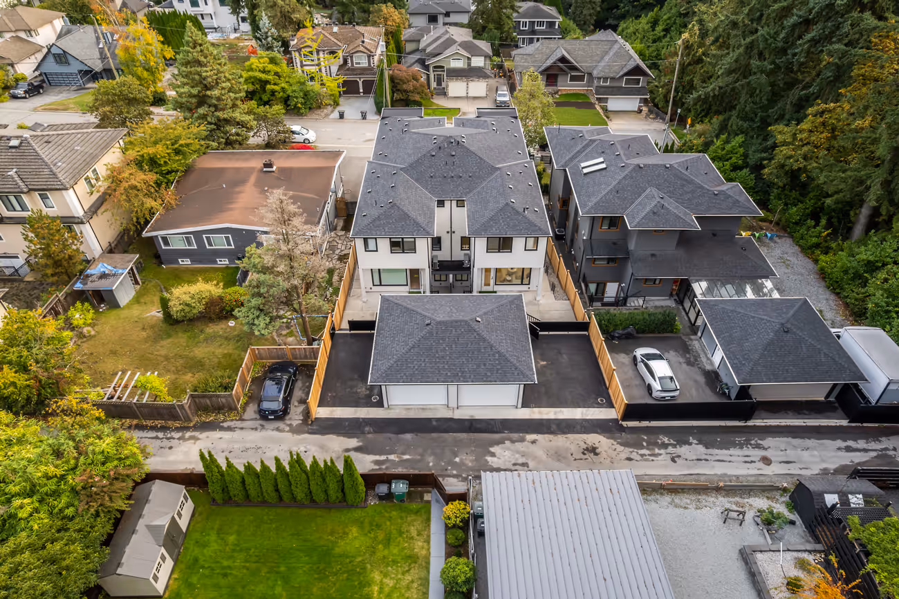 Aerial view of a residential neighborhood showing a modern townhouse complex with driveways and surrounding single-family homes and greenery.