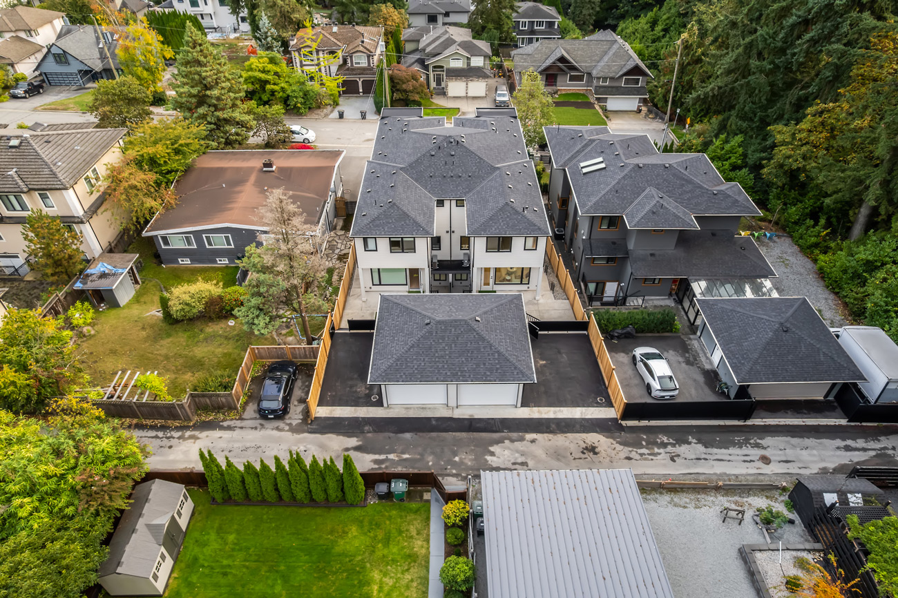 Aerial view of a residential neighborhood showing a modern townhouse complex with driveways and surrounding single-family homes and greenery.