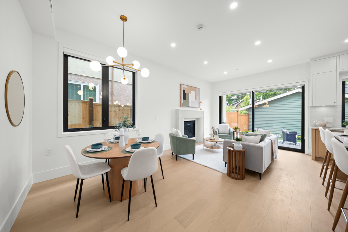Built by Asthan Homes in Burnaby, BC, Bright modern open-plan living and dining area with wooden floor, round dining table with four white chairs, and seating area with light green chairs and gray sofa.