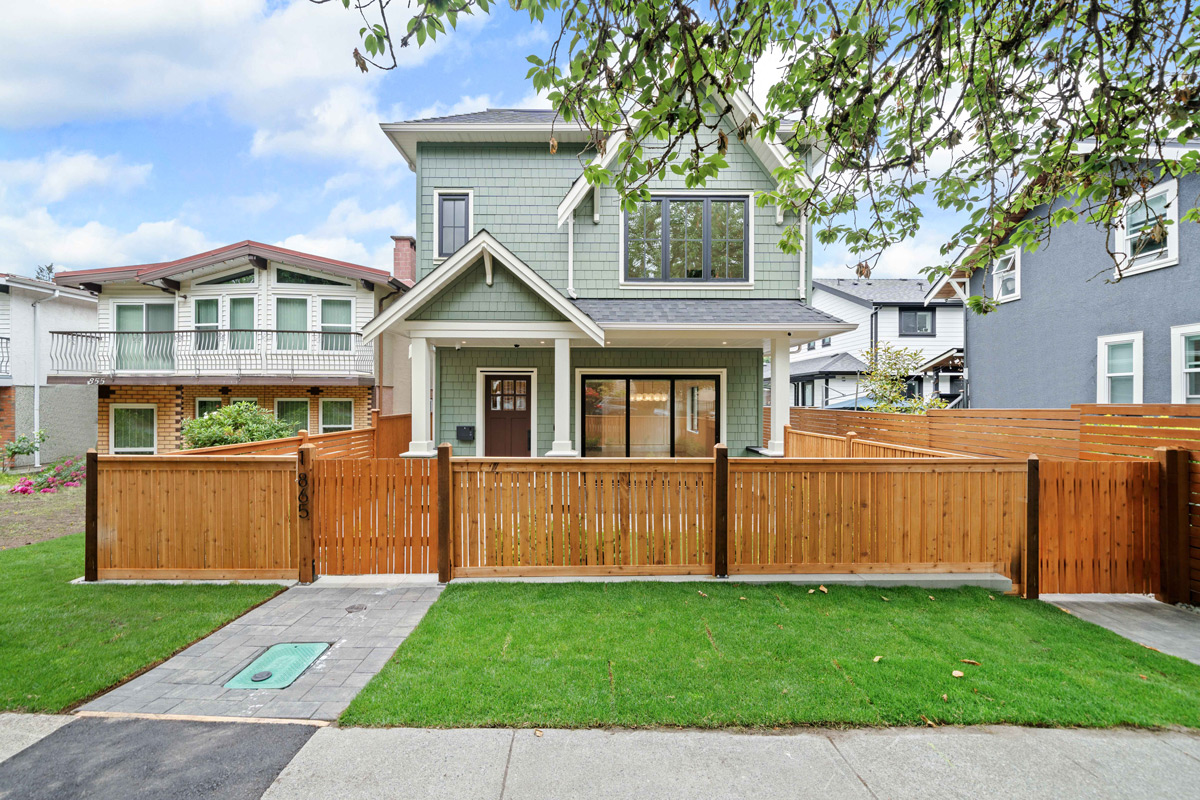 Built by Asthan Homes in Burnaby, BC, Two-story green house with wooden fence, green lawn, and walkway under a partly cloudy sky.