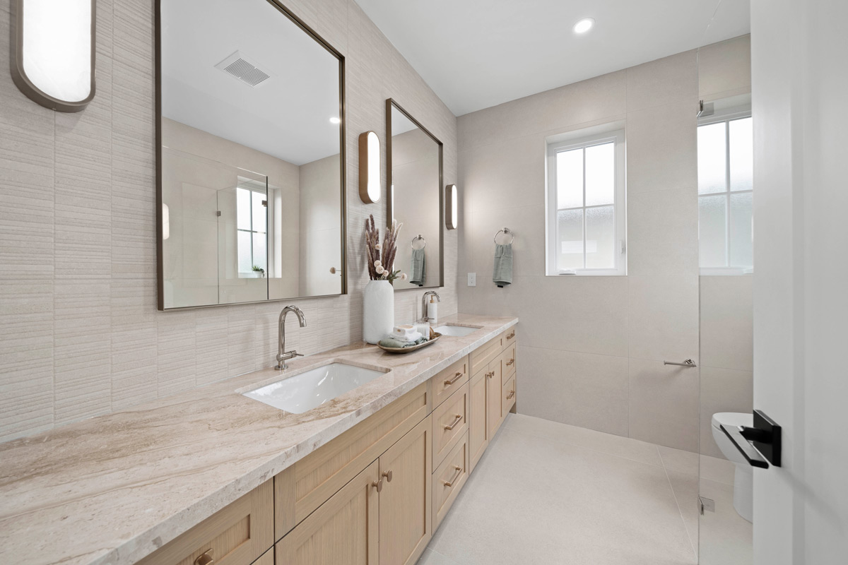 Built by Asthan Homes in Burnaby, BC, bathroom with double sink vanity, large mirrors, light wood cabinets, and a small frosted window.