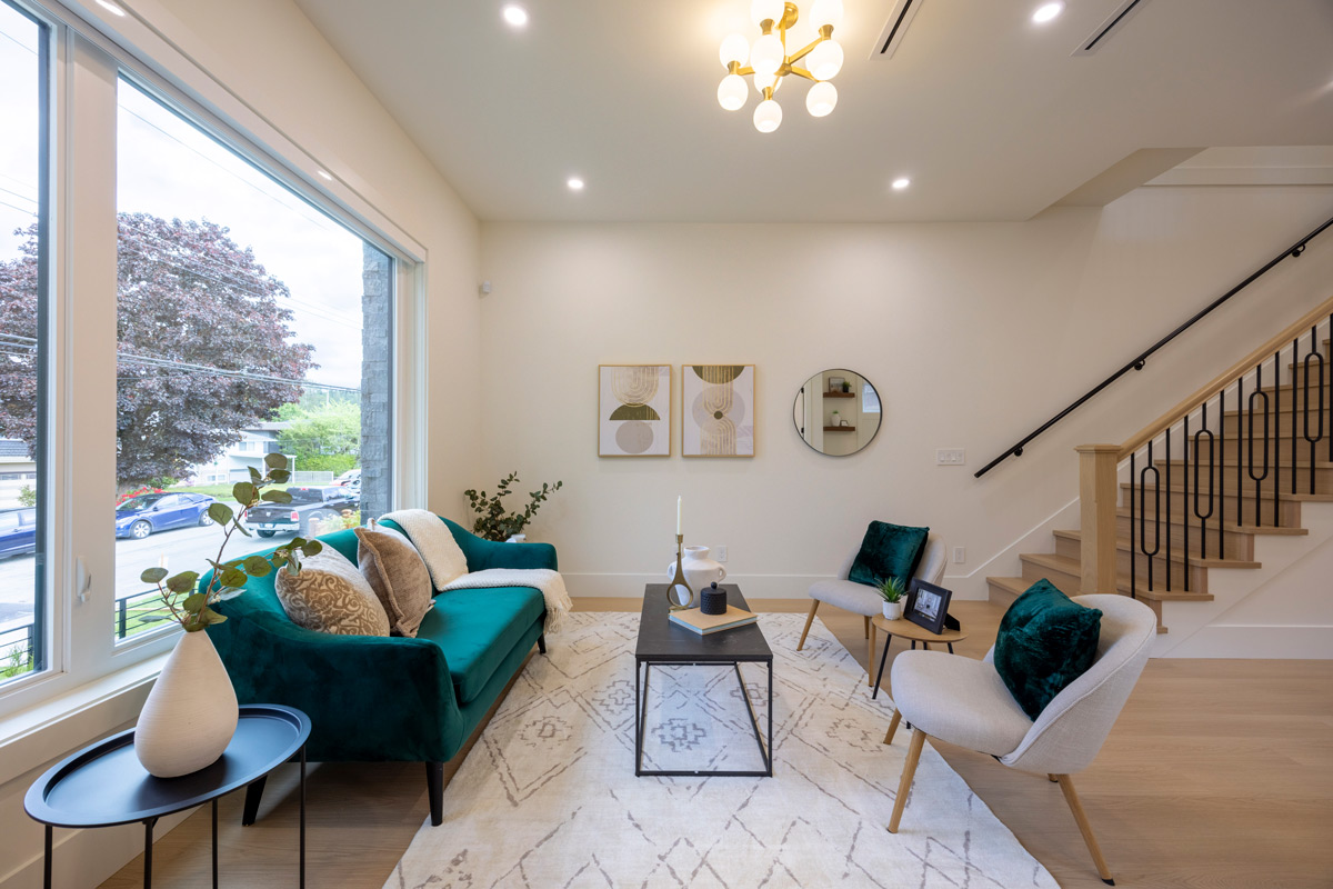 Built by Asthan Homes in Burnaby, BC, living room with teal velvet sofa, two beige armchairs with dark green pillows, a black coffee table, and large window.