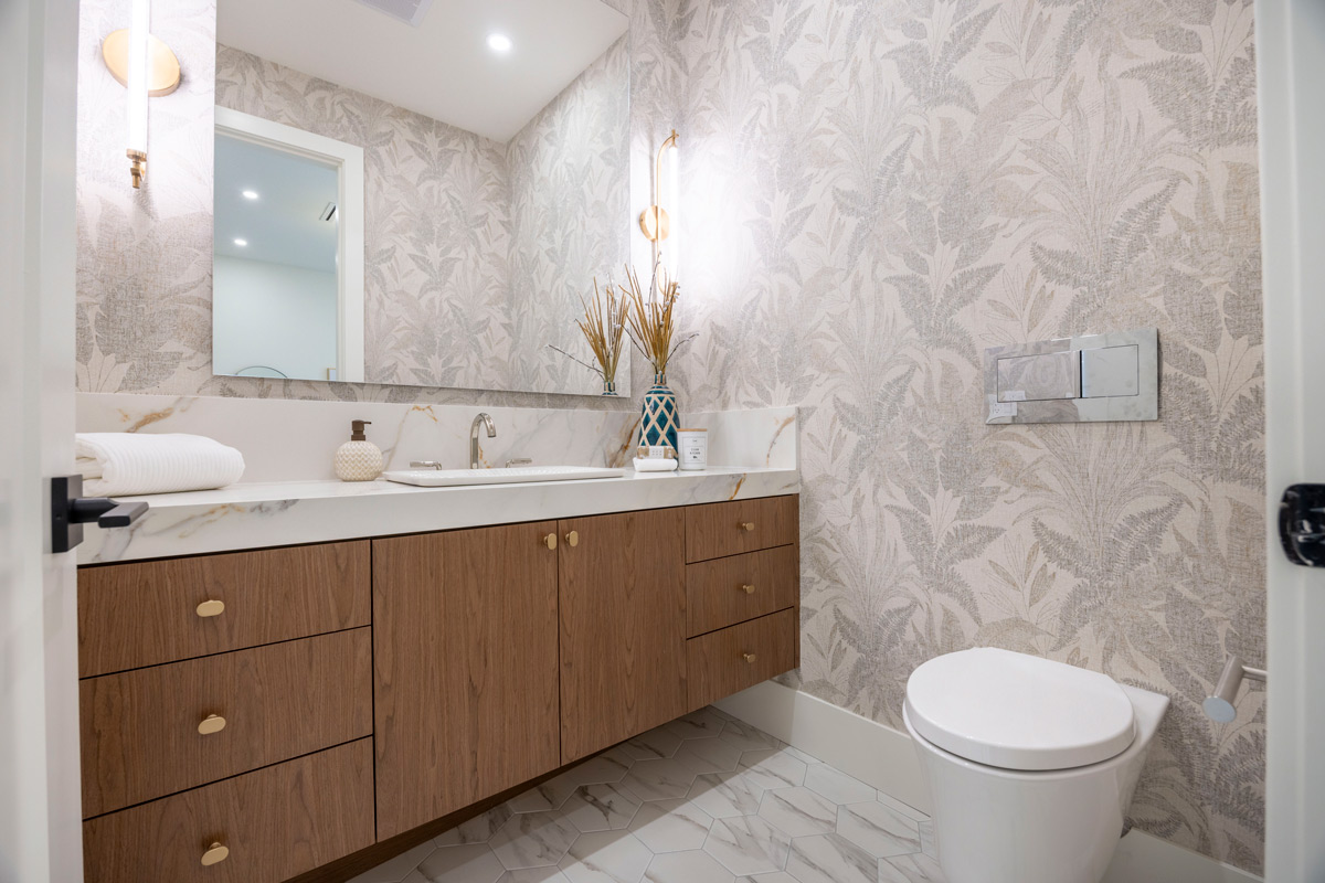 Built by Asthan Homes in Burnaby, BC, bathroom with wooden vanity, white marble countertop, large mirror, patterned wallpaper, and white toilet.